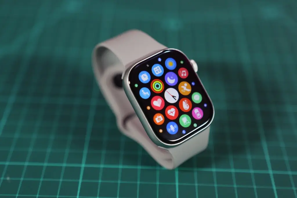 Smartwatch com grade de aplicativos coloridos sobre uma superfície verde.